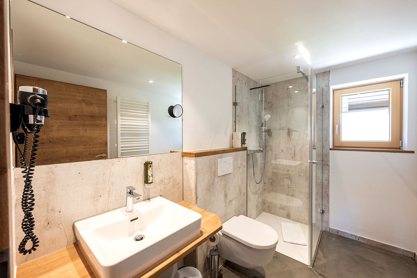 Badezimmer mit begehbarer Dusche, WC, Waschbecken, Spiegel, Fön und Fenster