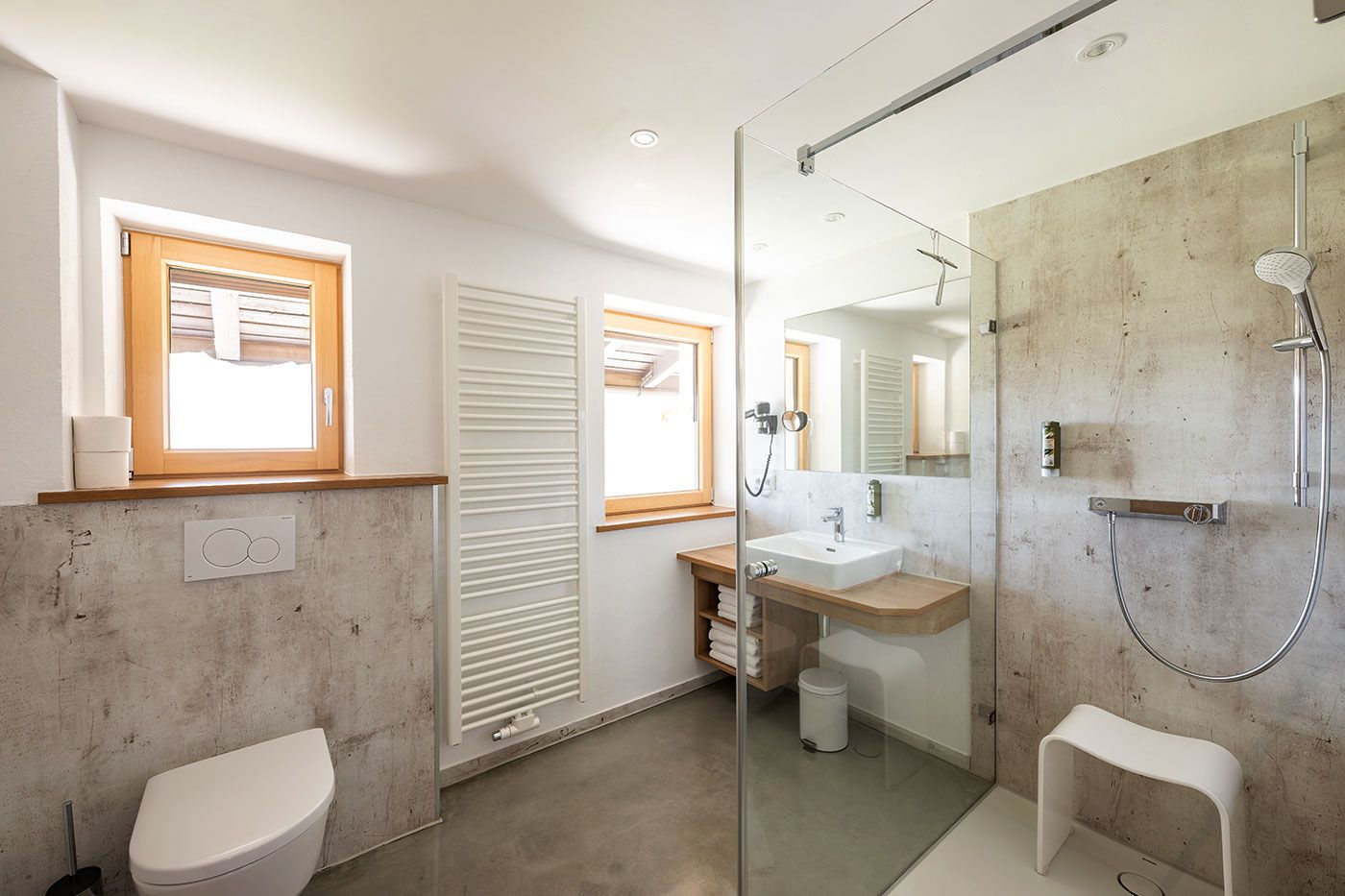 Helles Badezimmer mit Fenstern, WC, Waschbecken und begehbarer Dusche mit Hocker